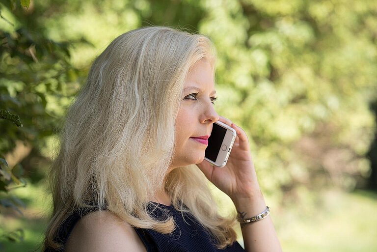 Eine Frau mittleren Alters, die gerade mit einem Smartphone einen Anruf tätigt.